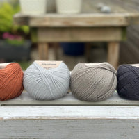 Four balls of wool in rust, silvery grey, medium grey, and dark grey. 