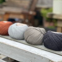 Four balls of wool in rust, silvery grey, medium grey, and dark grey. 