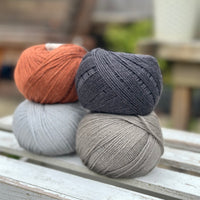 Four balls of wool in rust, silvery grey, medium grey, and dark grey. 