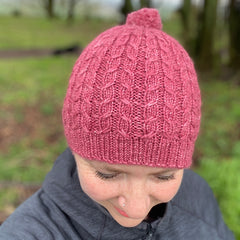 Victoria looking towards the floor wearing a pink knitted hat. The hat has a cable pattern and a small bobble on the crown