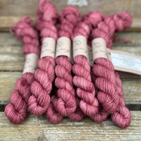 A pile of dark pink mini skeins with gold sparkle running through them