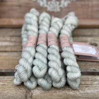 A pile of pale greenish grey mini skeins with gold sparkle running through them