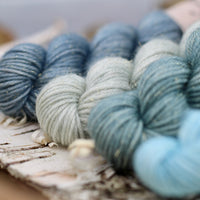 Four mini skeins of yarn in shades of blue/green with gold sparkle running through them