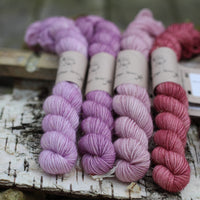 Four mini skeins of yarn with gold sparkle running through it. The skeins are in shades of pink and purple