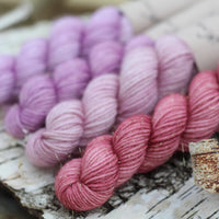 Four mini skeins of yarn with gold sparkle running through it. The skeins are in shades of pink and purple