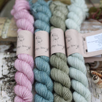 Four mini skeins of yarn with gold sparkle running through it. From left to right: a pink skein, a blue skein, a green skein and a pale green skein
