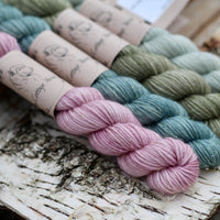 Four mini skeins of yarn with gold sparkle running through it. From left to right: a pink skein, a blue skein, a green skein and a pale green skein