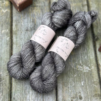 Two skeins of dark grey yarn with pale slubs running through them
