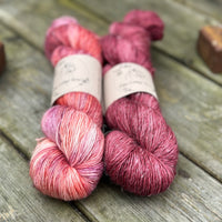 Two skeins of yarn in shades of reddish-purple, pink and orange