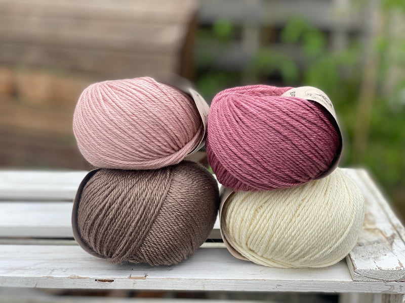 Four balls of yarn in two piles of two balls. On the left is a pink ball and a brown ball. On the right is a deep pink ball and a cream ball