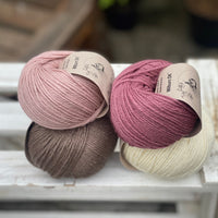 Four balls of yarn in two piles of two balls. On the left is a pink ball and a brown ball. On the right is a deep pink ball and a cream ball