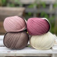 Four balls of yarn in two piles of two balls. On the left is a pink ball and a brown ball. On the right is a deep pink ball and a cream ball