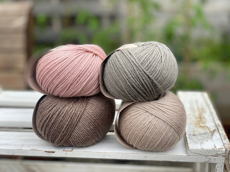 Four balls of yarn in two piles of two balls. On the left there is a pink ball and a brown ball. On the right there is a grey balls and a beige ball