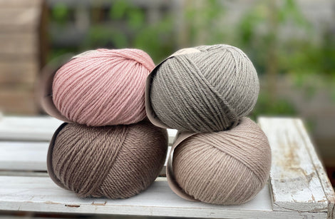 Four balls of yarn in two piles of two balls. On the left there is a pink ball and a brown ball. On the right there is a grey balls and a beige ball