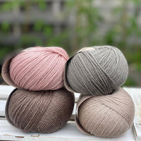 Four balls of yarn in two piles of two balls. On the left there is a pink ball and a brown ball. On the right there is a grey balls and a beige ball