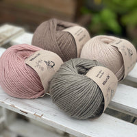 Four balls of yarn in two piles of two balls. On the left there is a pink ball and a brown ball. On the right there is a grey balls and a beige ball