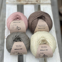 Four balls of yarn in two piles of two balls. On the left there is a pink ball and a grey ball. On the right there is a brown ball and a cream ball