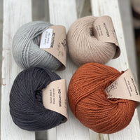 Four balls of yarn in two rows of two balls. On the left there is a pale blue ball and a dark grey ball. On the right there is a beige ball and a reddish brown ball