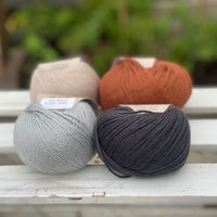 Four balls of yarn in two rows of two balls. On the left there is a beige ball and a pale blue ball. On the right there is a reddish brown ball and a dark grey ball