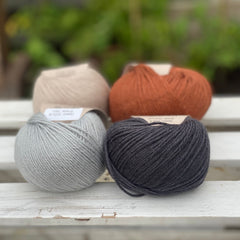 Four balls of yarn in two rows of two balls. On the left there is a beige ball and a pale blue ball. On the right there is a reddish brown ball and a dark grey ball