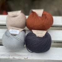 Four balls of yarn in two rows of two balls. On the left there is a beige ball and a pale blue ball. On the right there is a reddish brown ball and a dark grey ball