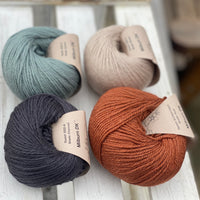 Four balls of yarn in two rows of two balls. On top row left there is a beige ball and a pale blue ball. On the bottom row there is a reddish brown ball and a dark grey ball