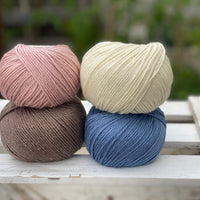 Four balls of yarn in two rows of two balls. There is a pink ball, a cream ball, a brown ball and a blue ball