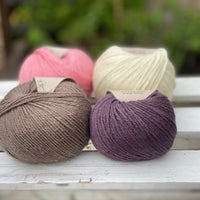 Four balls of yarn in two rows of two balls. There is a bright pink ball, a cream ball, a brown ball and a dark purple ball