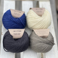 Four balls of yarn in two rows of two balls. There is a deep blue ball, a cream ball, a grey ball and a dark grey ball