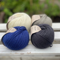 Four balls of yarn in two rows of two balls. There is a deep blue ball, a cream ball, a grey ball and a dark grey ball