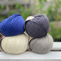Four balls of yarn in two rows of two balls. There is a deep blue ball, a cream ball, a grey ball and a dark grey ball