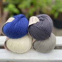 Four balls of yarn in two rows of two balls. There is a deep blue ball, a cream ball, a grey ball and a dark grey ball