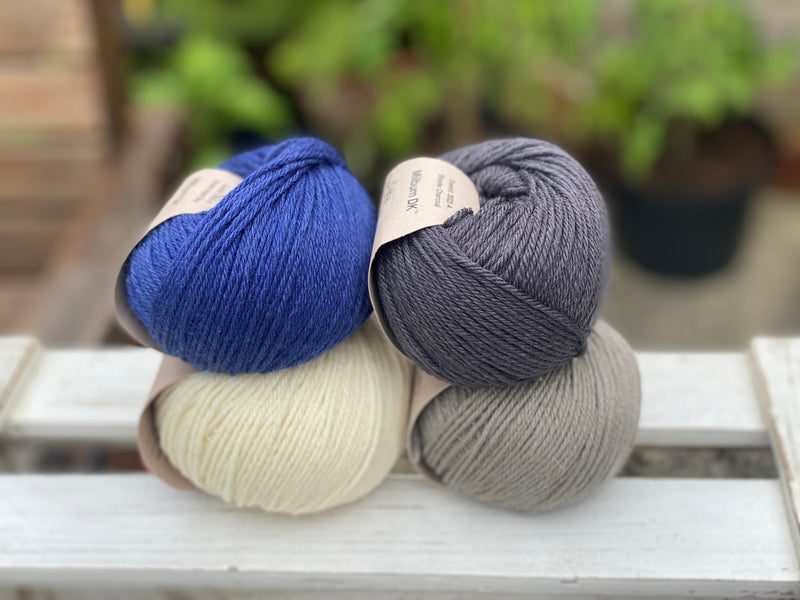 Four balls of yarn in two rows of two balls. There is a deep blue ball, a cream ball, a grey ball and a dark grey ball