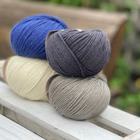 Four balls of yarn in two rows of two balls. There is a deep blue ball, a cream ball, a grey ball and a dark grey ball