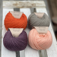 Four balls of yarn in two rows of two balls. There is an orange ball, a dark purple ball, a grey ball and a peachy orange ball