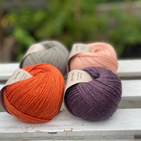 Four balls of yarn in two rows of two balls. There is an orange ball, a dark purple ball, a grey ball and a peachy orange ball