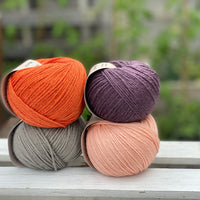 Four balls of yarn in two rows of two balls. There is an orange ball, a dark purple ball, a grey ball and a peachy orange ball