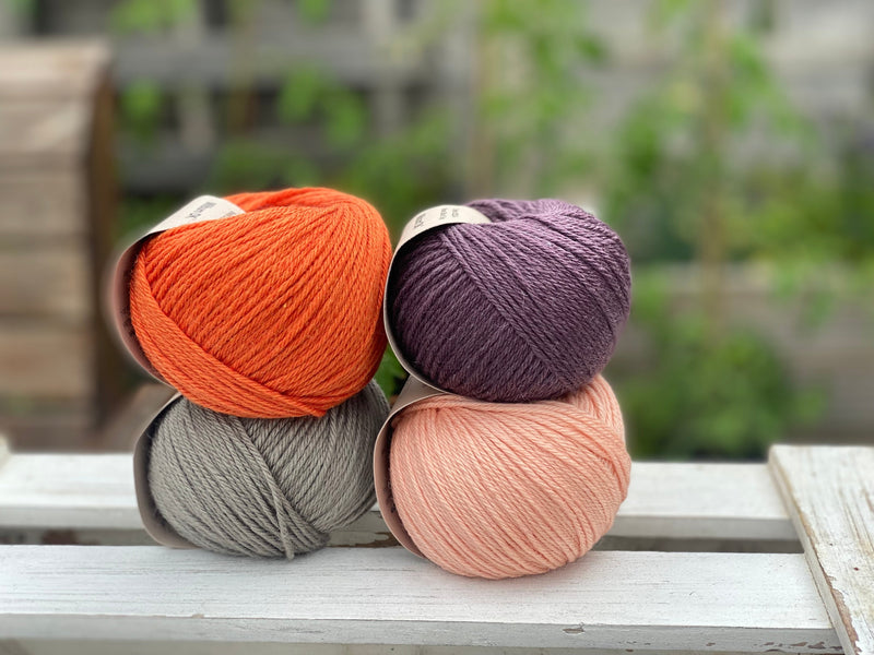 Four balls of yarn in two rows of two balls. There is an orange ball, a dark purple ball, a grey ball and a peachy orange ball