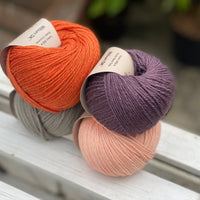 Four balls of yarn in two rows of two balls. There is an orange ball, a dark purple ball, a grey ball and a peachy orange ball