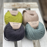 Four balls of yarn in two rows of two. There is a green ball, a dark grey ball, a beige ball and a blue-green ball.