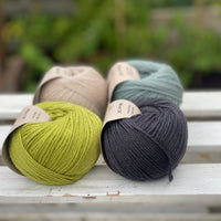 Four balls of yarn in two rows of two. There is a green ball, a dark grey ball, a beige ball and a blue-green ball.