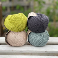 Four balls of yarn in two rows of two. There is a green ball, a dark grey ball, a beige ball and a blue-green ball.