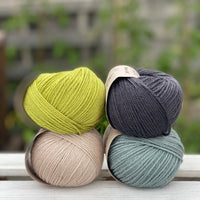 Four balls of yarn in two rows of two. There is a green ball, a dark grey ball, a beige ball and a blue-green ball.
