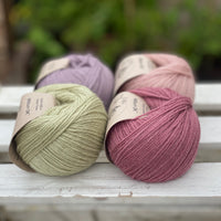 Four balls of yarn in two rows of two. There is a pale purple ball, a light pink ball, a light green ball and a dark pink ball.