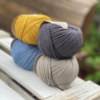 Four balls of yarn in two rows of two. There is a yellow ball, a dark grey ball, a blue ball and a grey ball.
