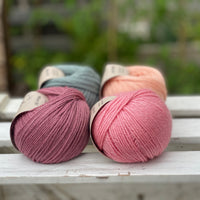 Four balls of yarn in two rows of two. There is a blue-green ball, a peachy orange ball, a dark pink ball and a bright pink ball.