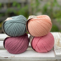 Four balls of yarn in two rows of two. There is a blue-green ball, a peachy orange ball, a dark pink ball and a bright pink ball.