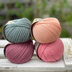 Four balls of yarn in two rows of two. There is a blue-green ball, a peachy orange ball, a dark pink ball and a bright pink ball.