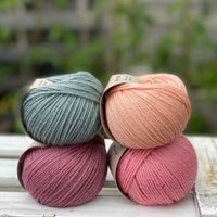 Four balls of yarn in two rows of two. There is a blue-green ball, a peachy orange ball, a dark pink ball and a bright pink ball.