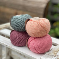 Four balls of yarn in two rows of two. There is a blue-green ball, a peachy orange ball, a dark pink ball and a bright pink ball.